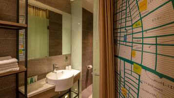Un bany modern amb un mirall gran, un lavabo i una zona de dutxa. Hi ha tovalloles a una estant i un mapa a la paret.