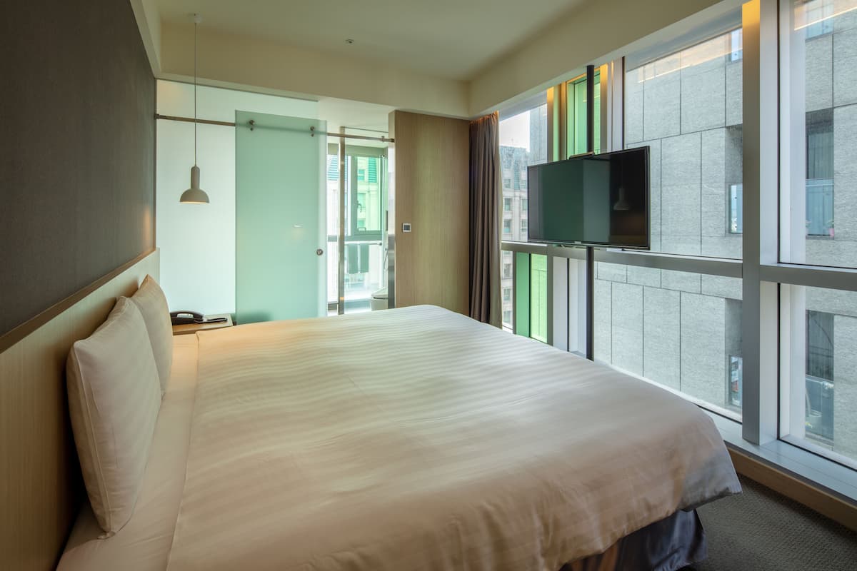 Quarto de hotel com cama grande, televisão na parede e janela vista para a cidade.