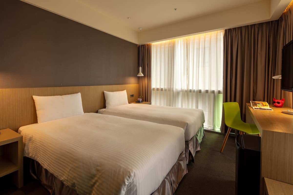 Quarto de hotel com duas camas, uma escrivaninha, uma cadeira e uma televisão.