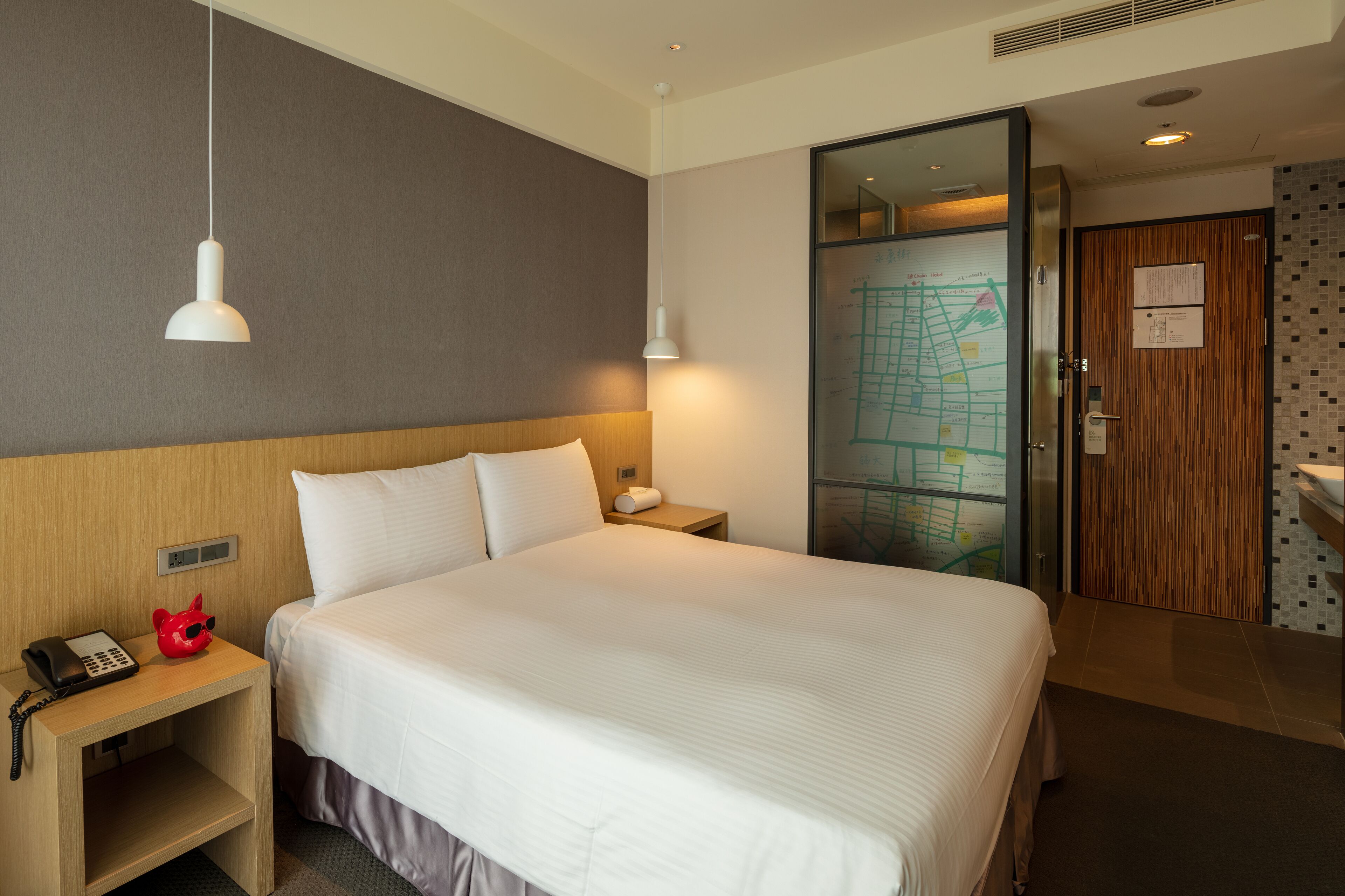Habitación de hotel con una cama grande, una mesita de noche con un teléfono, una lámpara y un mapa en la pared.