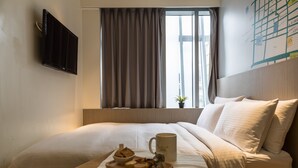 Een hotelkamer met een bed, een dienblad met snacks, een mok en een tv aan de muur.