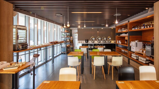 Een modern café met houten tafels en stoelen, een bar met flessenplanken, en een keuken op de achtergrond.