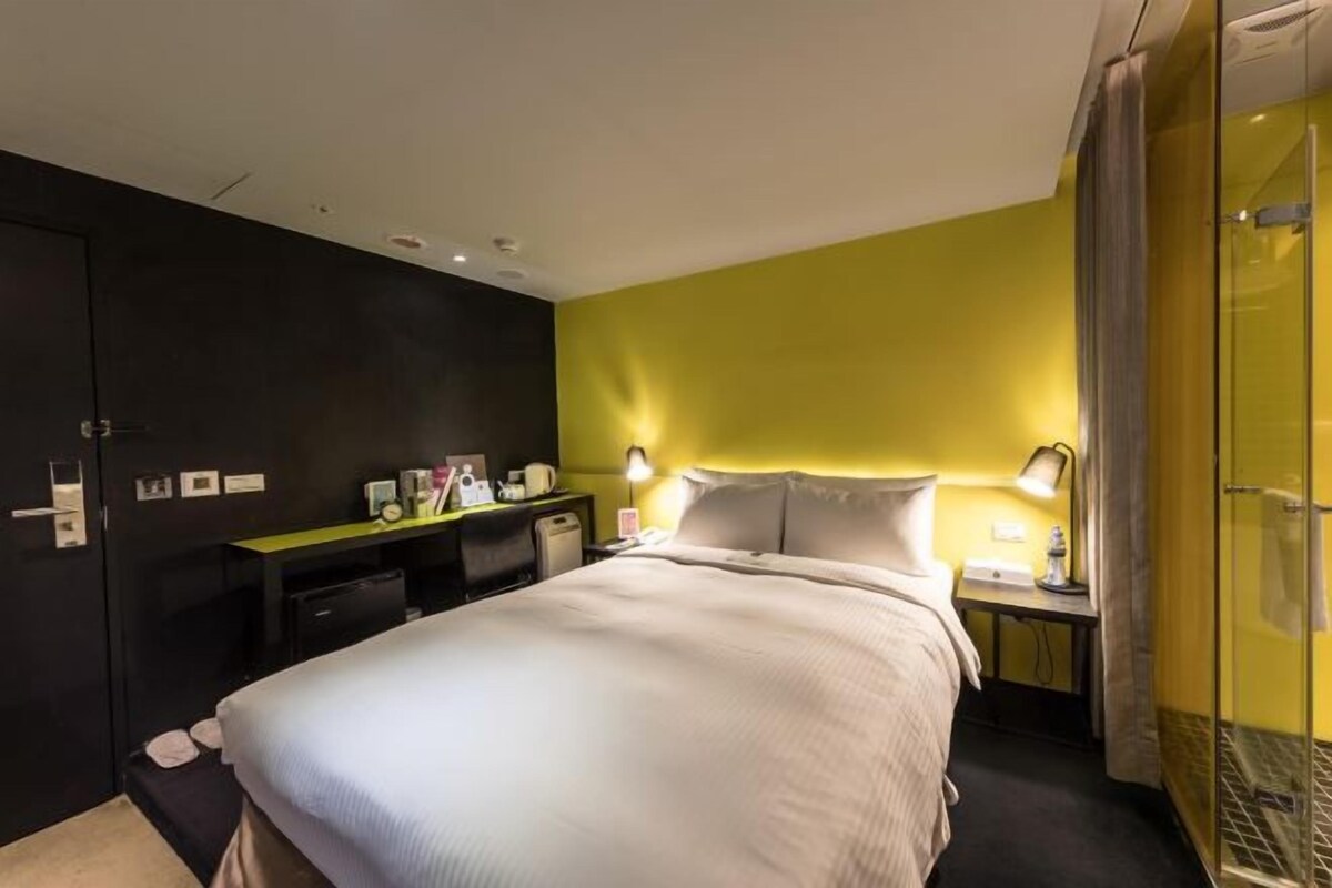 Ein Hotelzimmer mit einem Bett, einem Nachttisch, einer Lampe und einem Schreibtisch mit Stuhl.