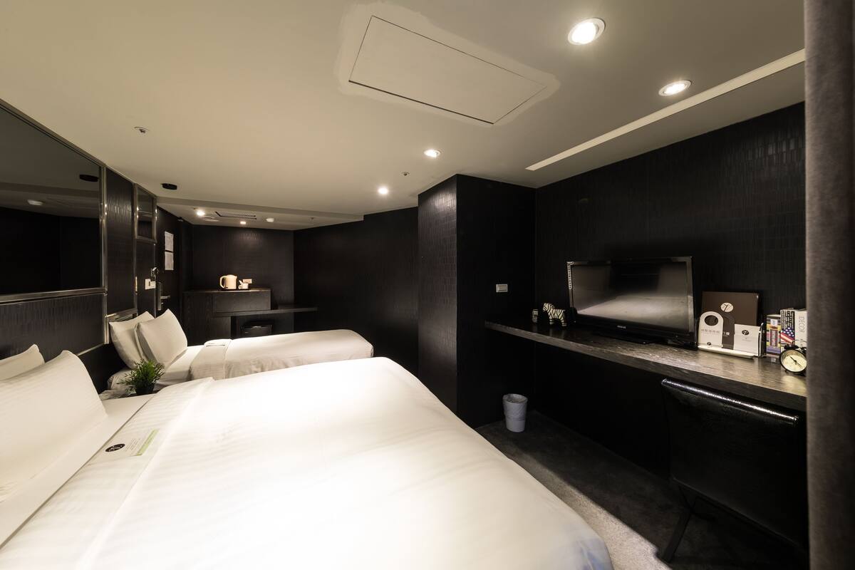 A modern hotel room with two beds, a TV, a desk, and a small plant.