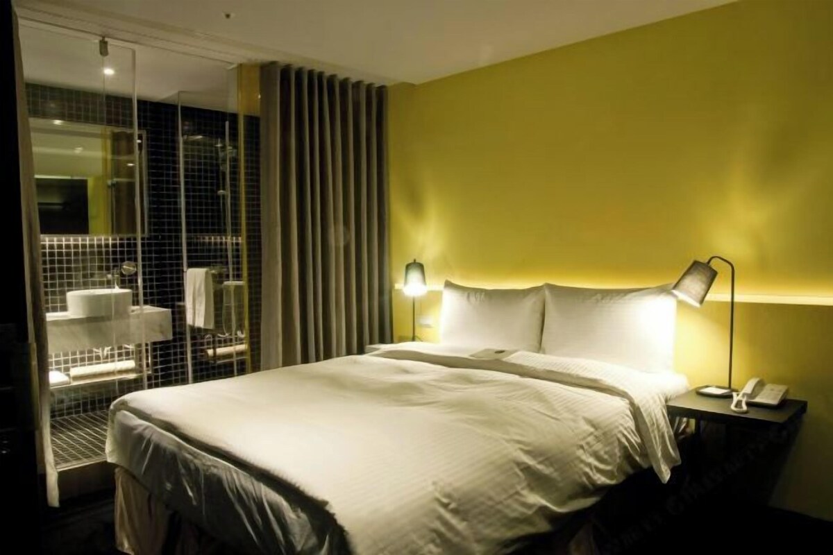 Een hotelkamer met een bed, nachtkastje, lamp en een badkamer met douche en toilet.