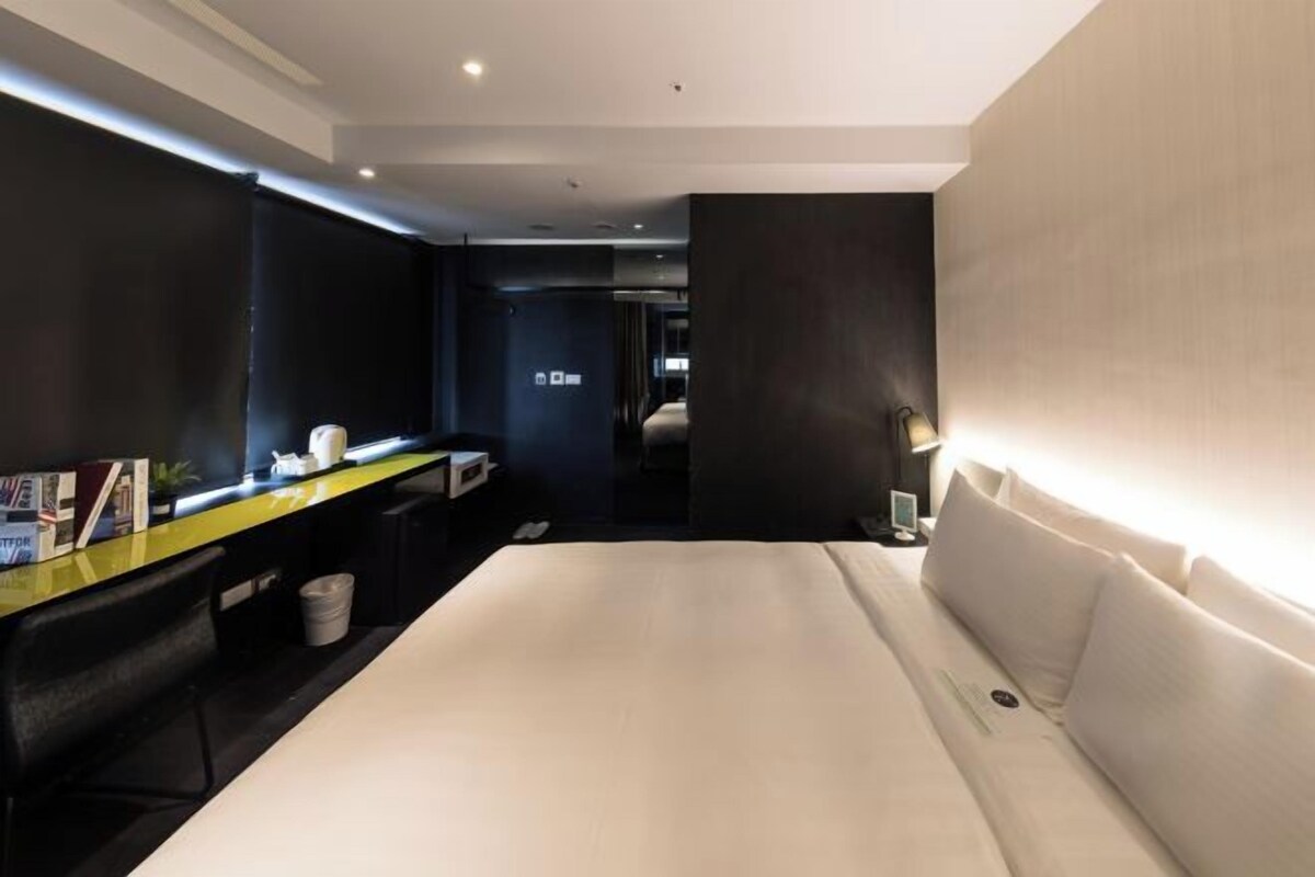 Ein modernes Hotelzimmer mit einem großen Bett, einem Schreibtisch mit Computer und einer kleinen Sitzecke.