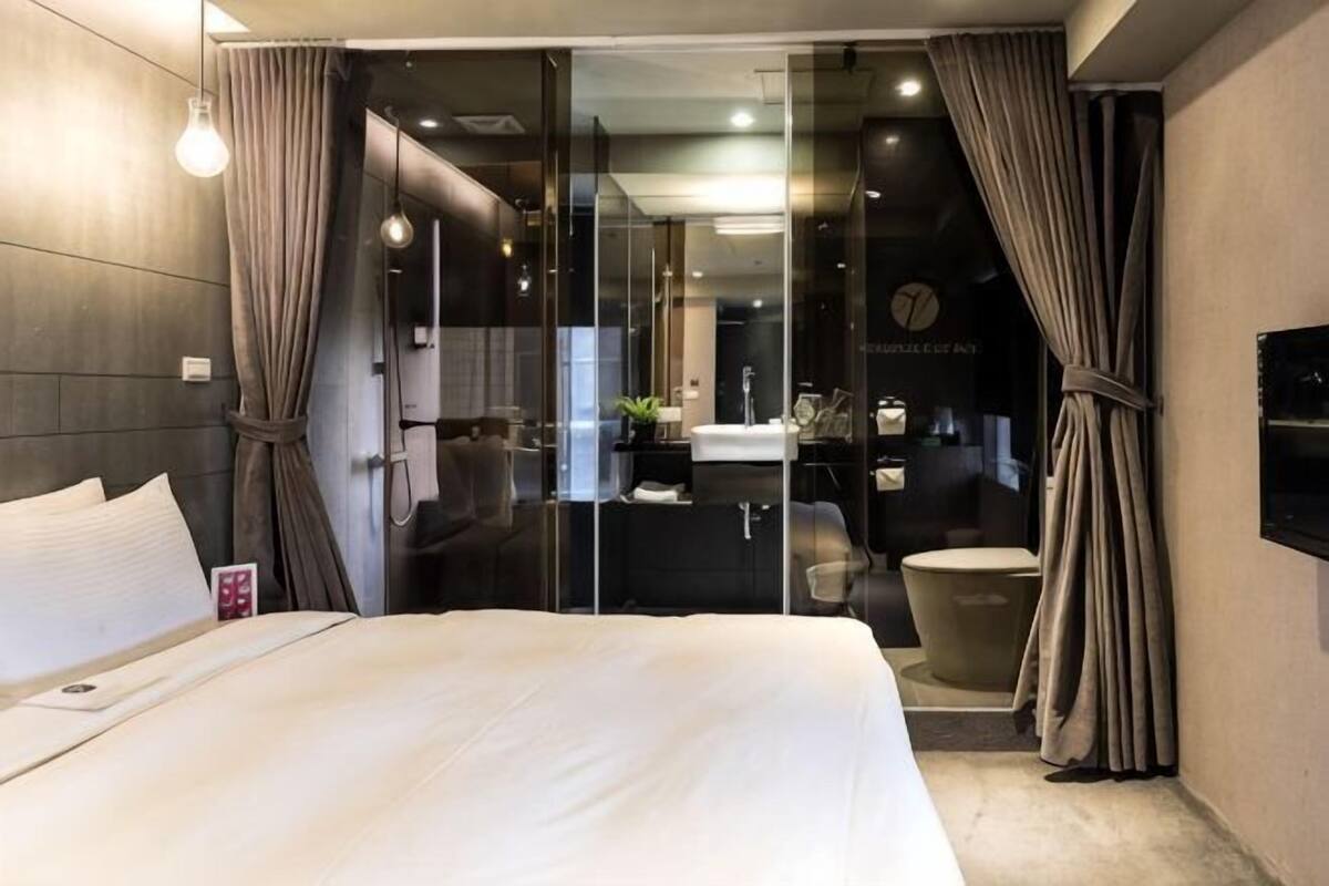A modern hotel room with a large bed, a glass shower enclosure, and a separate bathroom with a bathtub.
