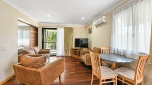 Una sala de estar moderna con un juego de sofá, una mesa de comedor con sillas, un televisor de pantalla plana y ventanas amplias con cortinas translúcidas.