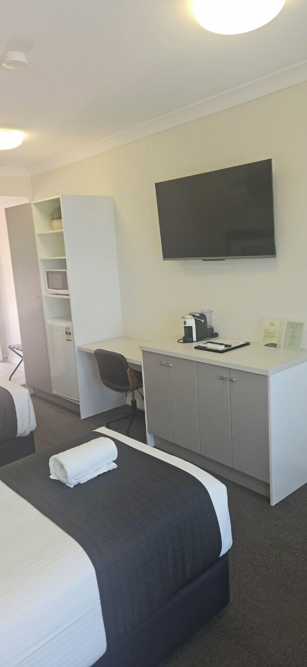 Una habitación de hotel con cama, escritorio con silla, televisor y minibar.