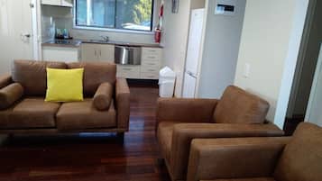 A compact living space with a brown sofa set, a kitchen area with a stainless steel sink, and a white refrigerator.