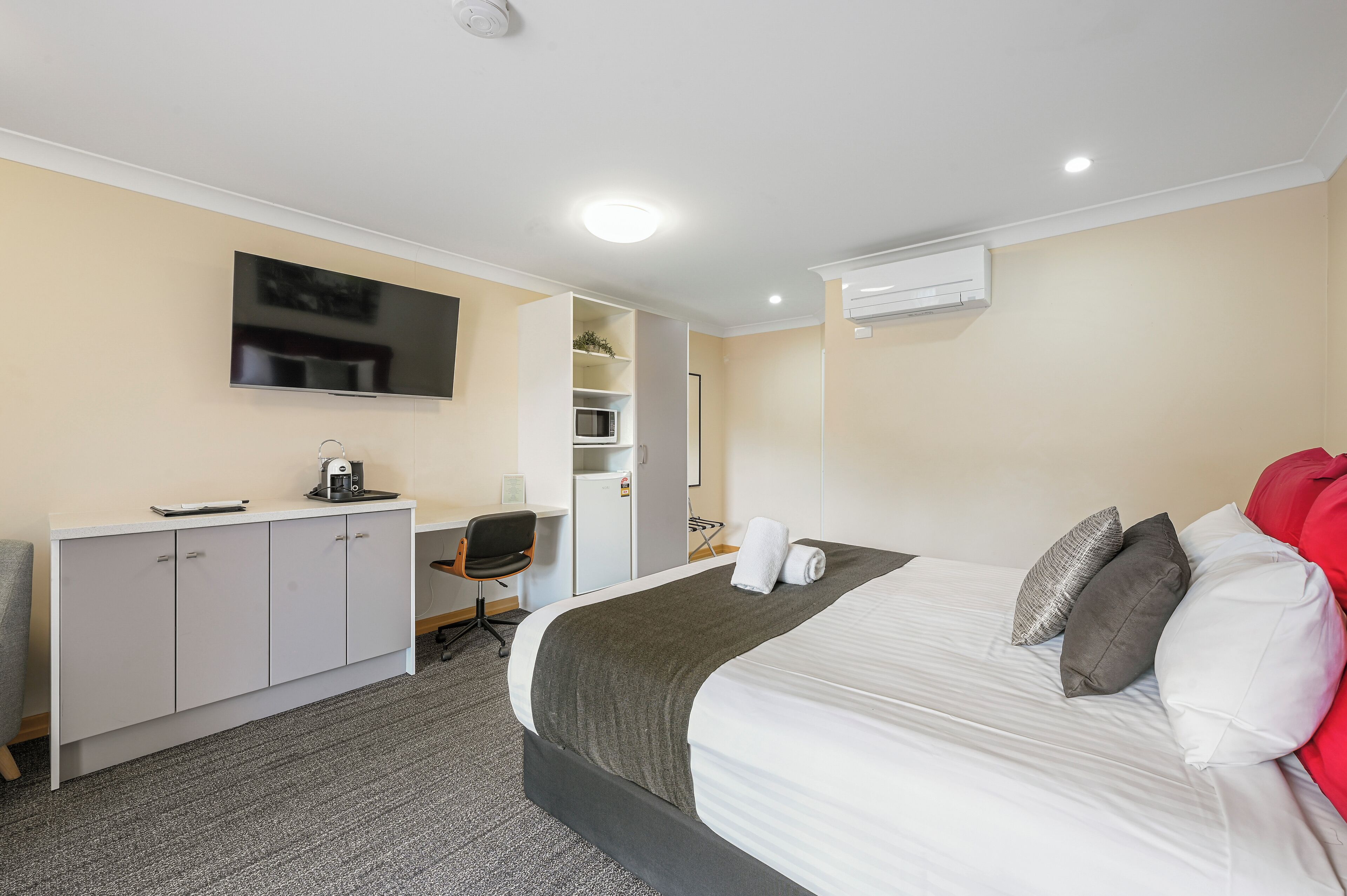 A hotel room with a bed, a desk, a chair, a TV, and an air conditioning unit.