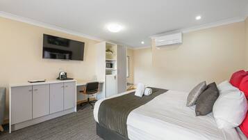 A hotel room with a bed, a desk, a chair, a TV, and an air conditioning unit.