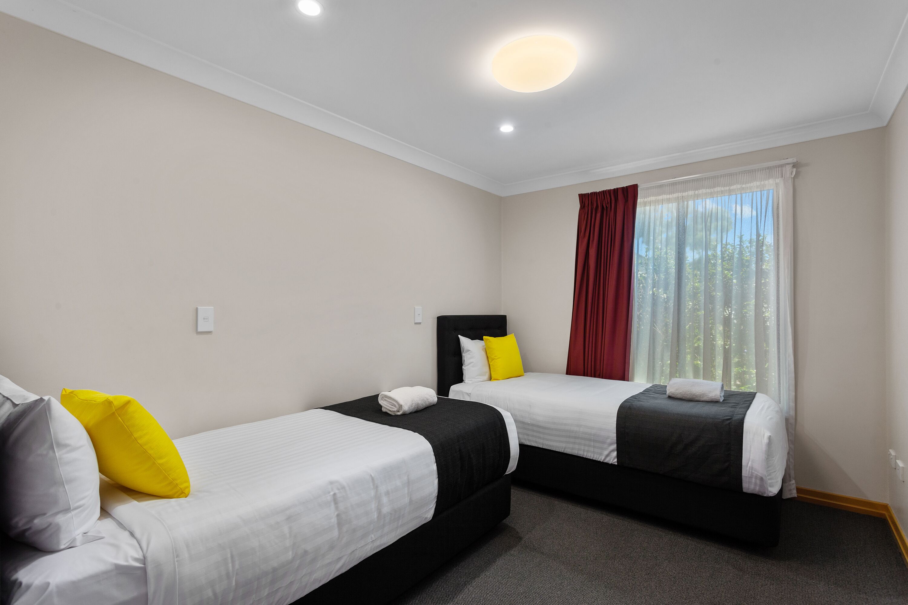 A hotel room with two single beds, a large window with curtains, and a ceiling light.