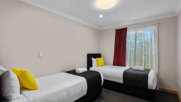 A hotel room with two single beds, a large window with curtains, and a ceiling light.