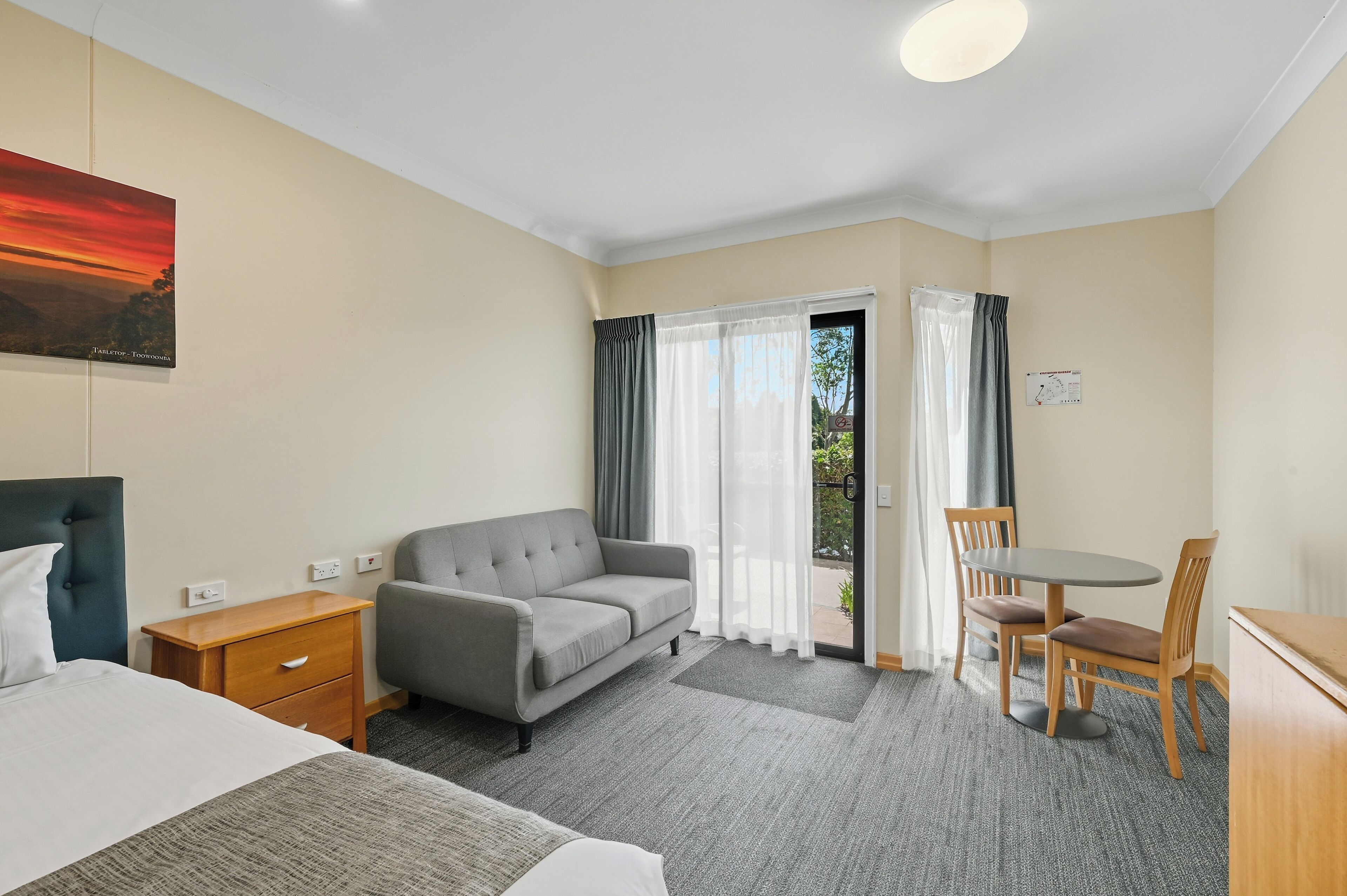 Une chambre d’hôtel avec un lit, un canapé, une petite table et une chaise. Il y a une fenêtre avec des rideaux et une vue sur l’extérieur.