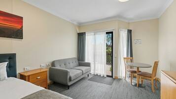 Une chambre d’hôtel avec un lit, un canapé, une petite table et une chaise. Il y a une fenêtre avec des rideaux et une vue sur l’extérieur.