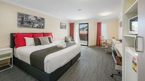 Habitación de hotel con cama, escritorio, silla, televisión y ventana con cortinas.