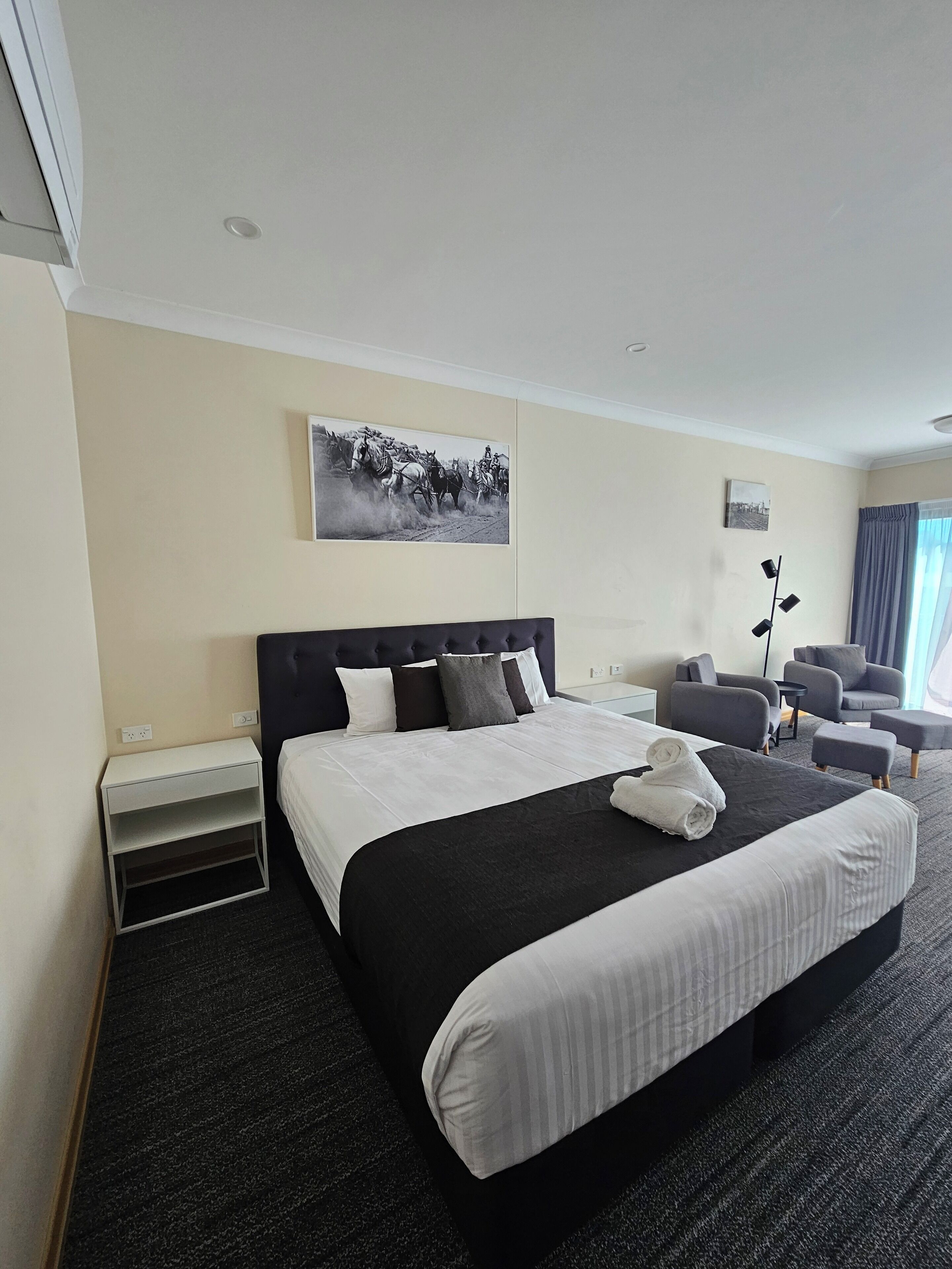 A hotel room with a large bed, a nightstand, a desk, two armchairs, and a floor lamp.