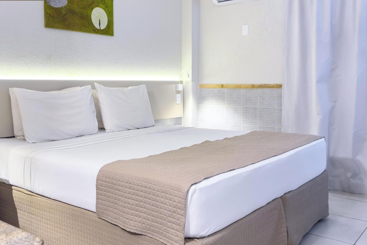 A neatly made bed with white linens and a beige blanket, a wooden chair, and a small table with a menu or pamphlet.