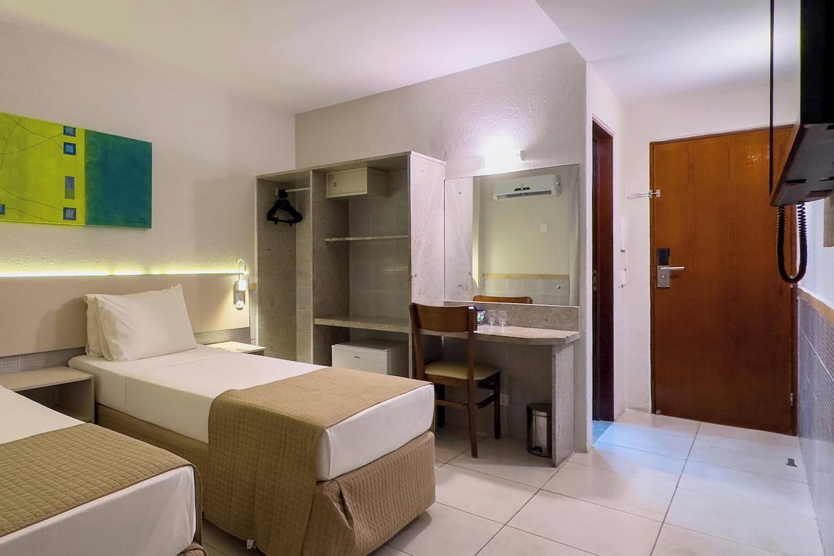 A hotel room with two beds, a desk, a chair, a mirror, and a green abstract painting on the wall.