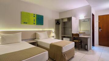 Quarto de hotel com duas camas, uma escrivaninha, uma cadeira, um espelho e um quadro abstrato verde na parede.