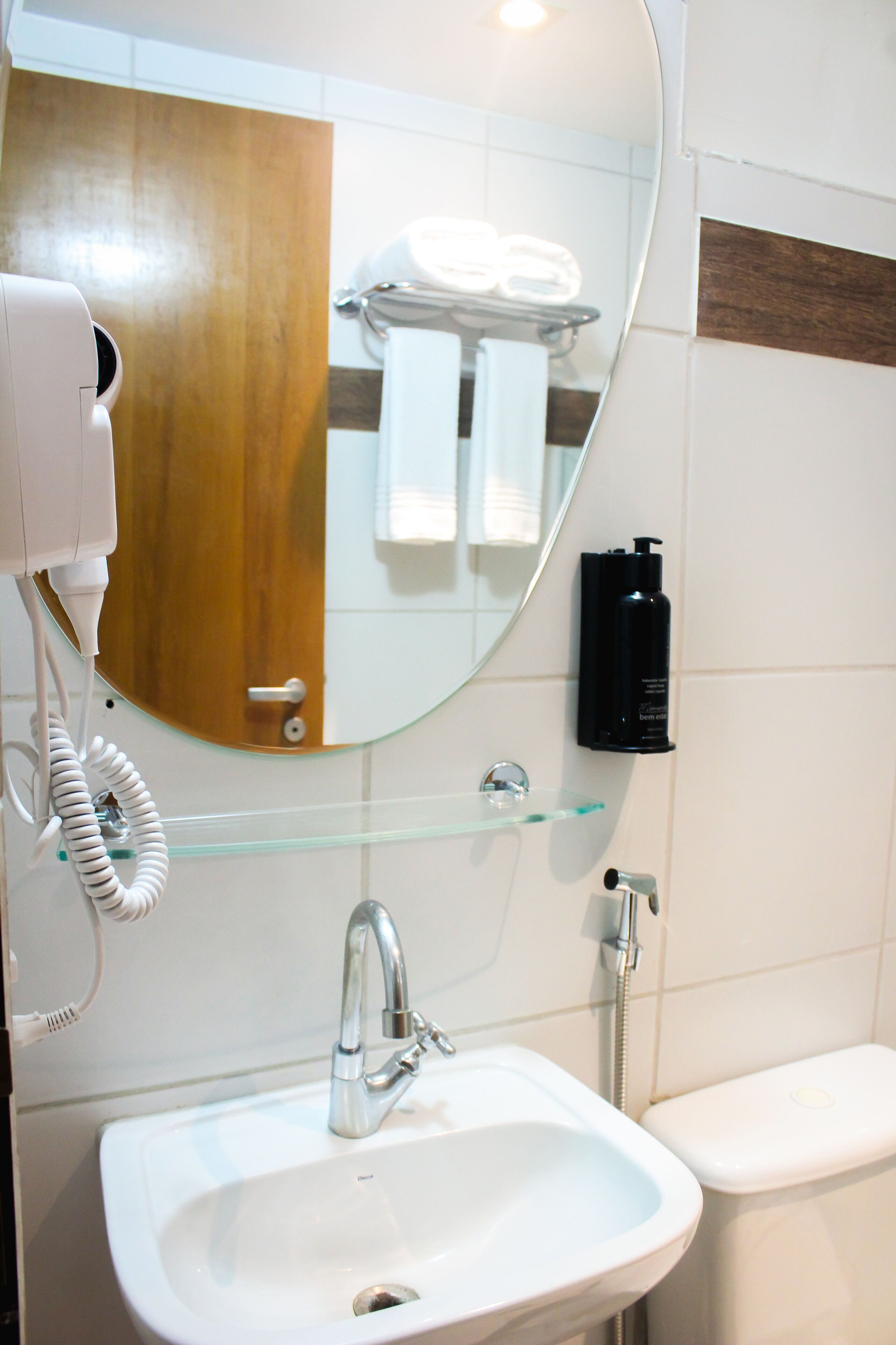 A bathroom with a white sink, a mirror, a hairdryer, and a glass shelf with toiletries.