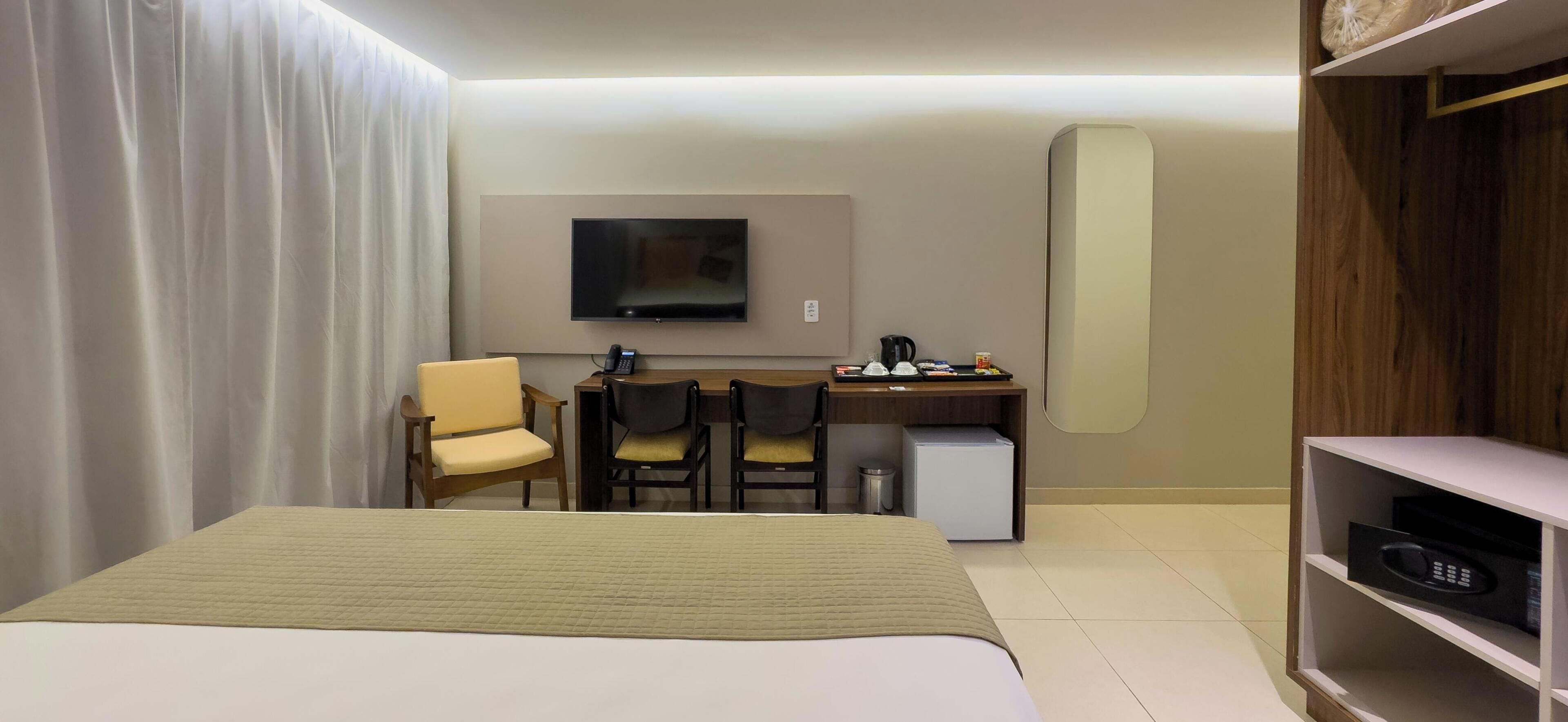 Ein Hotelzimmer mit einem Bett, einem Schreibtisch mit zwei Stühlen, einem Fernseher, einer Kaffeemaschine und einem kleinen Kühlschrank.