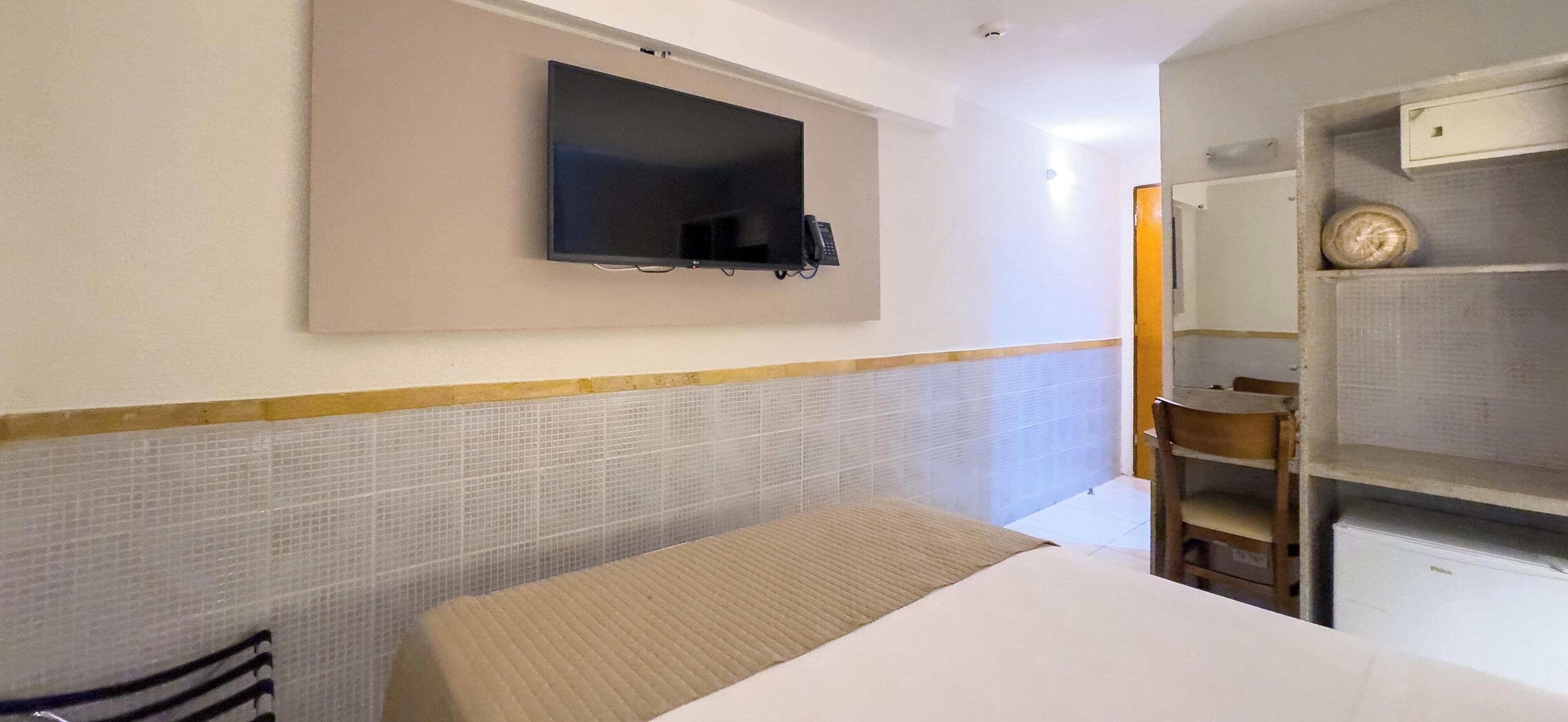A hotel room with a bed, a TV mounted on the wall, a small desk, and a chair.