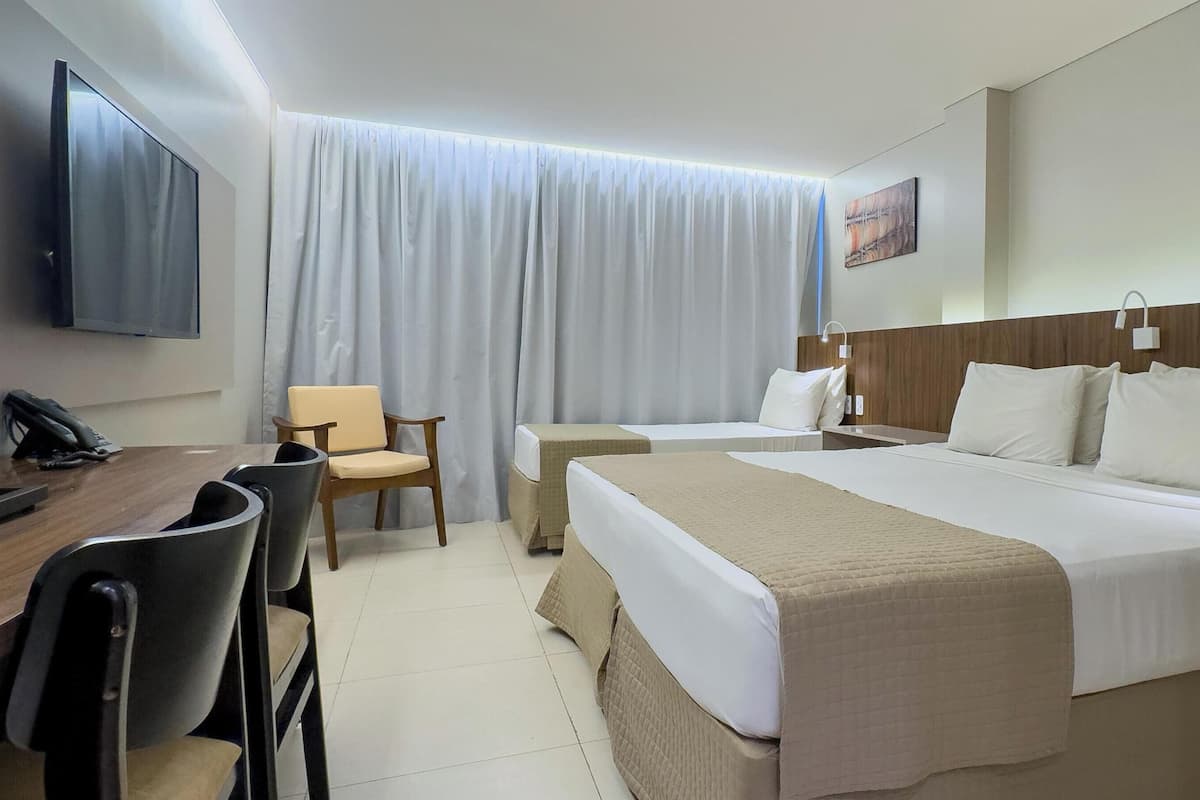 A hotel room with a bed, two bedside tables, a desk with a chair, a television, and a window with curtains.