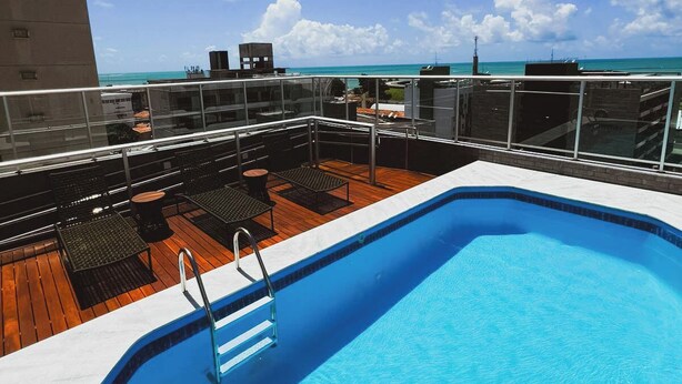 A rooftop pool with a clear view of the ocean, surrounded by lounge chairs and tables.