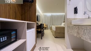 A hotel room with a minibar, a desk with a chair, a bed, a bathroom with a sink and mirror, and a TV mounted on the wall.