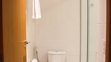 Un baño pequeño y limpio con inodoro, cabina de ducha de vidrio y un cubo de basura.
