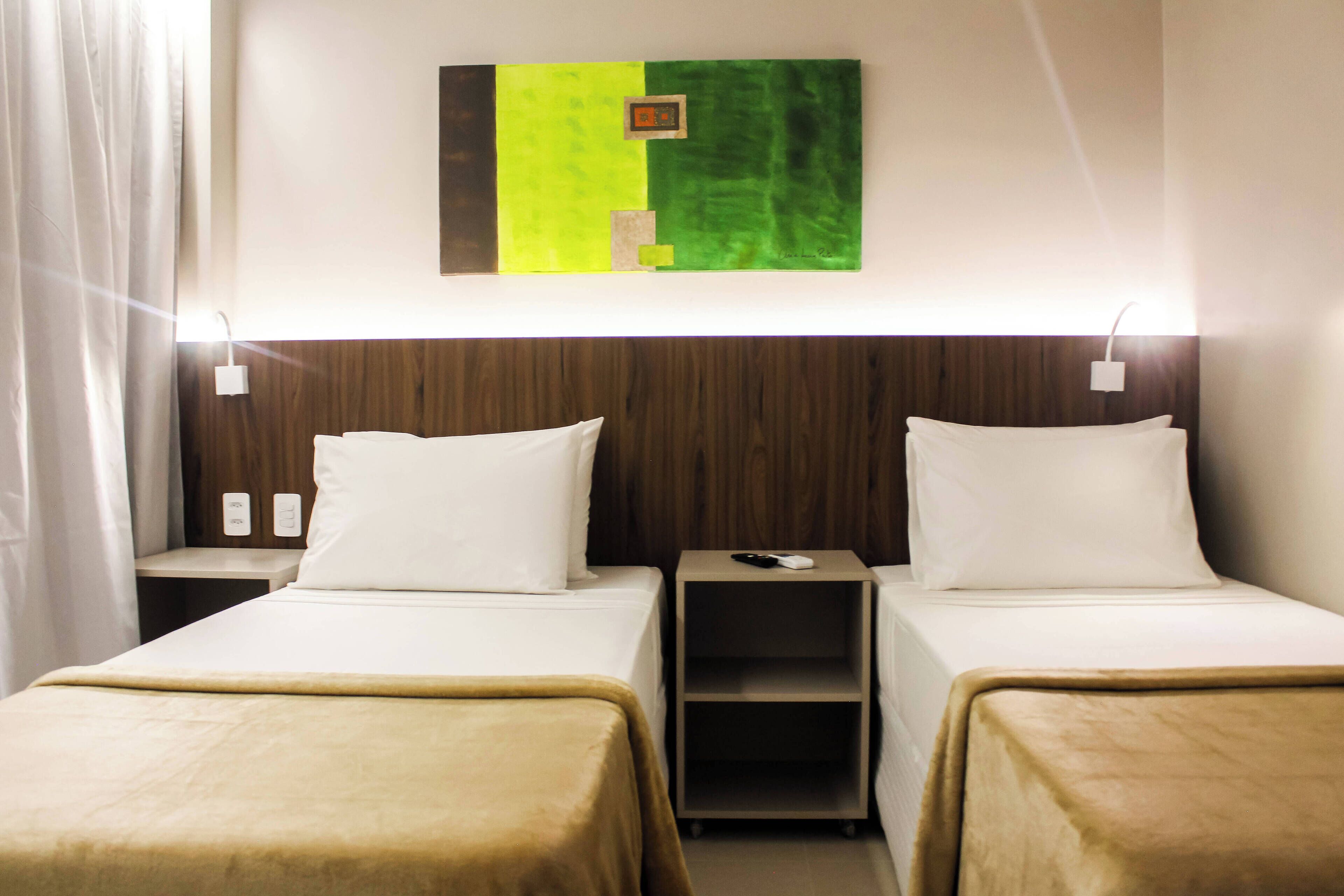 Ein Hotelzimmer mit zwei Betten, einem Nachttisch mit Telefon und Fernbedienung sowie einem Wandbild.