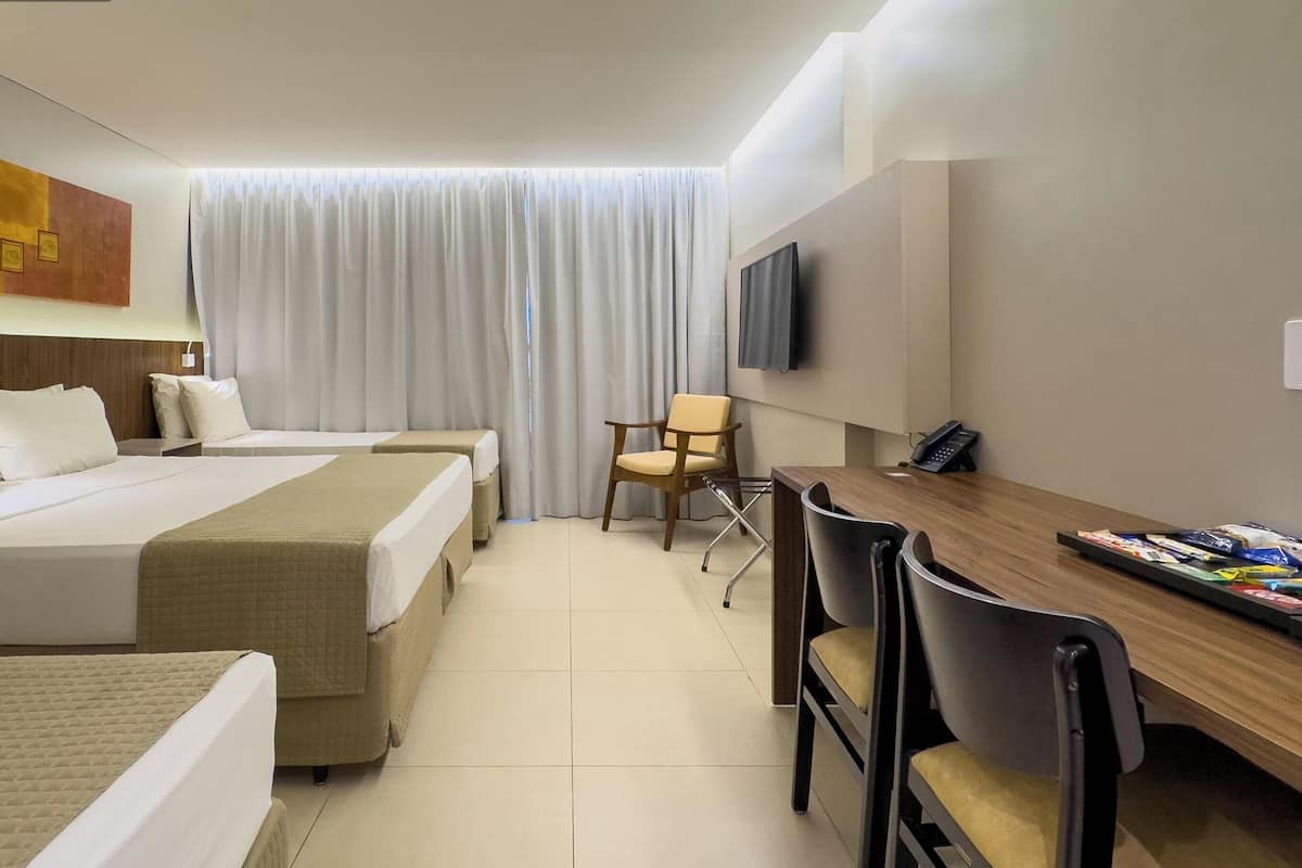 A hotel room with two beds, a desk, a chair, a TV, and a window with curtains.