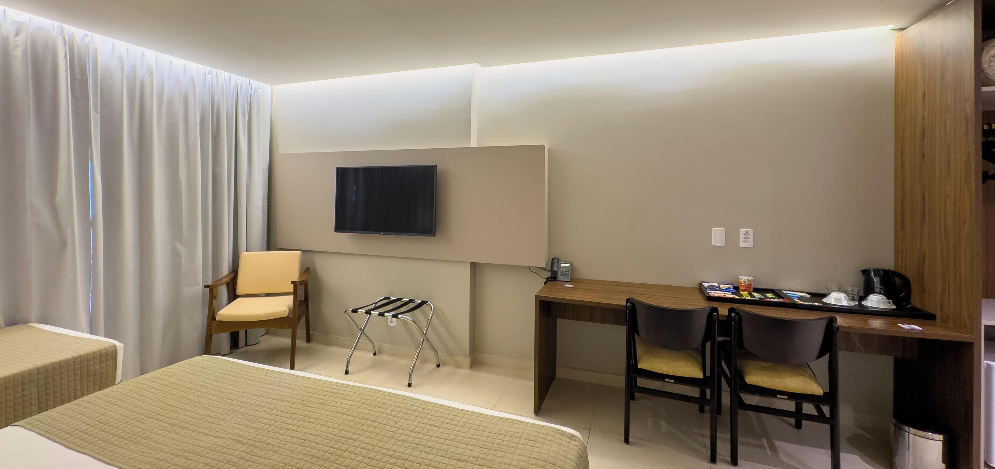 Habitación de hotel con cama, escritorio, silla, televisión y una mesita con tetera y tazas.