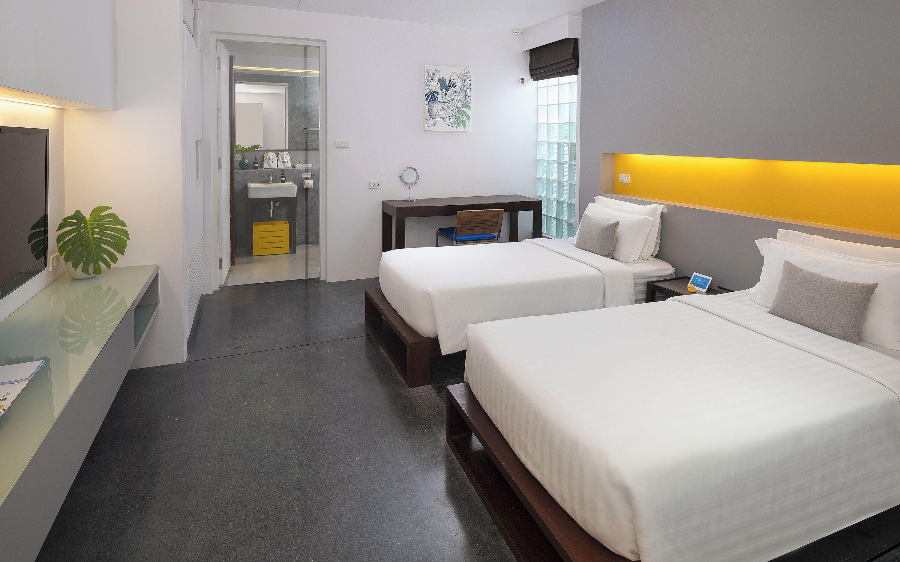A hotel room with two beds, a desk, a chair, a small table, and a potted plant.