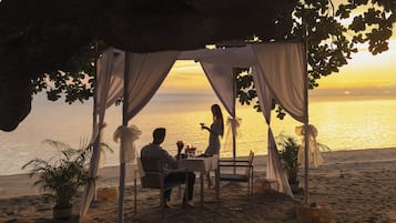 Un entorno de playa con una toldilla y una mesa bajo un árbol, con vista al mar.