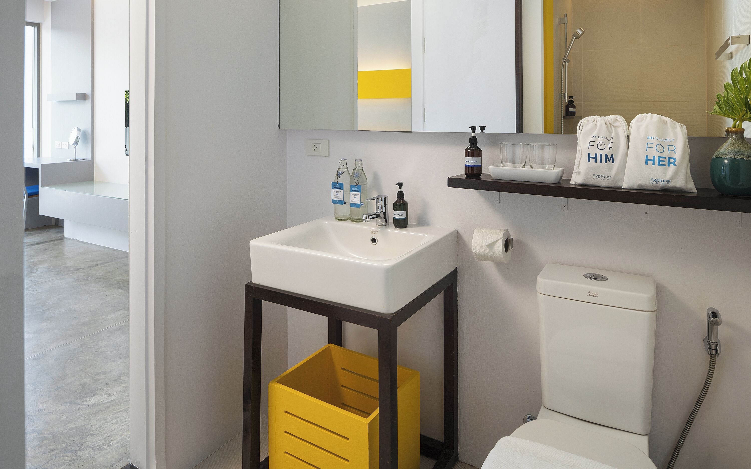 Une salle de bain moderne avec un lavabo blanc, un bac de rangement jaune, des toilettes et une étagère contenant des articles de toilette.