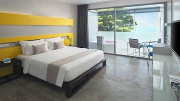 A modern hotel room with a large bed, a nightstand, a desk with a chair, and a balcony with a view of the ocean.