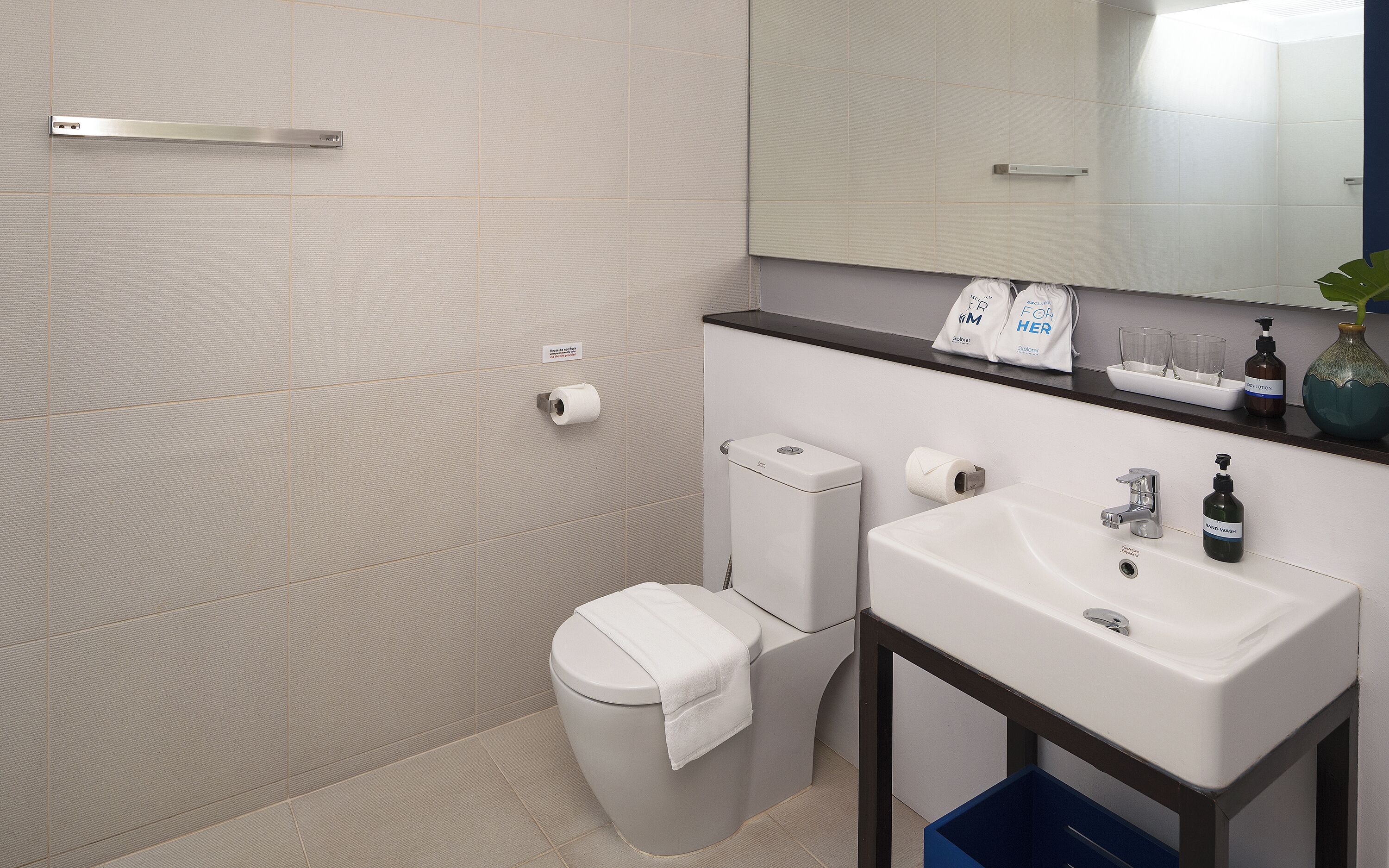 A modern bathroom with a toilet, sink, and mirror. There are toiletries and a towel on the sink.