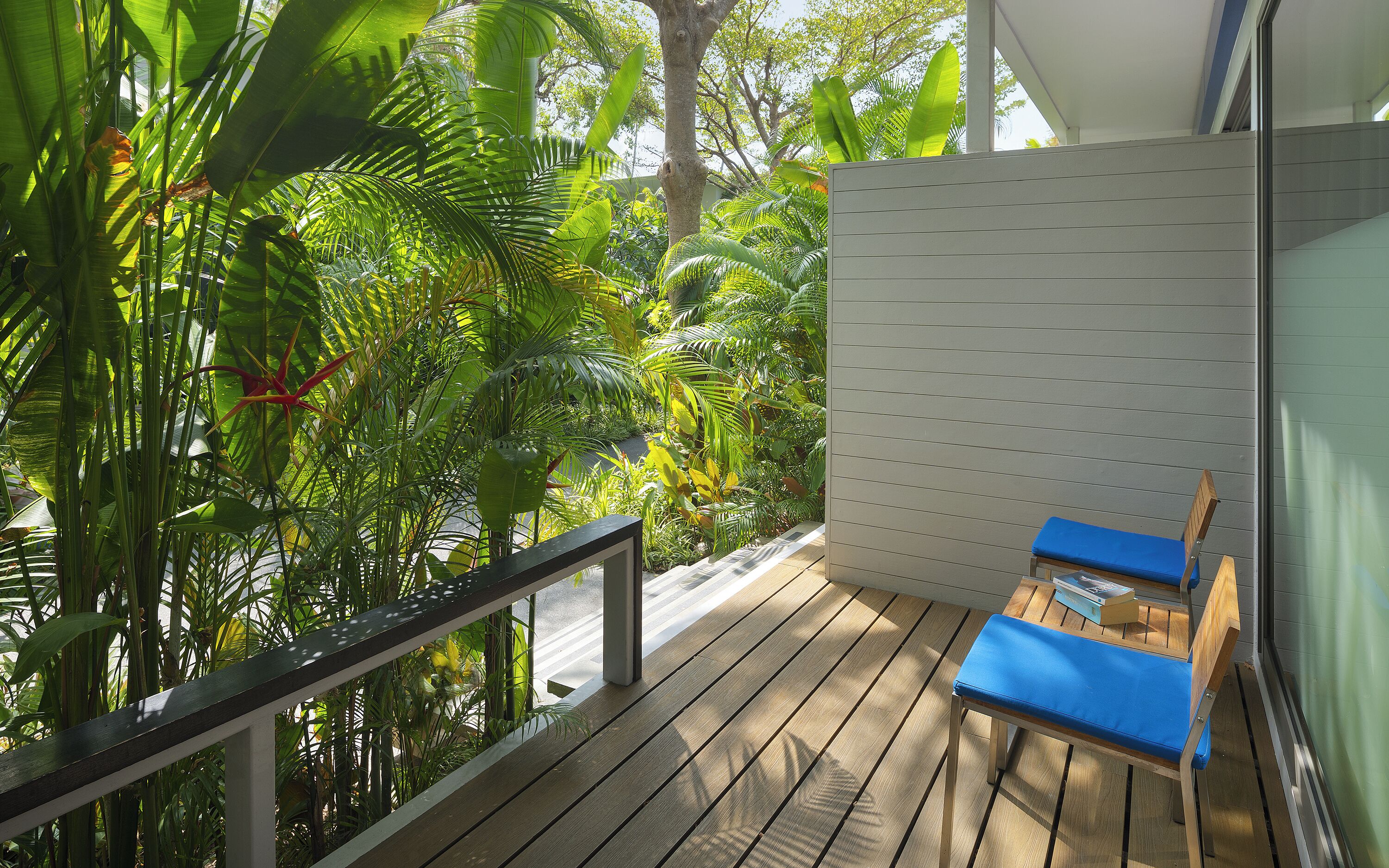 Un balcón con suelo de madera, un sillón con cojines azules y una pared blanca con líneas horizontales.