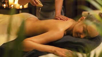 Iemand ontvangt een massage in een kamer met weinig licht en kaarsen.