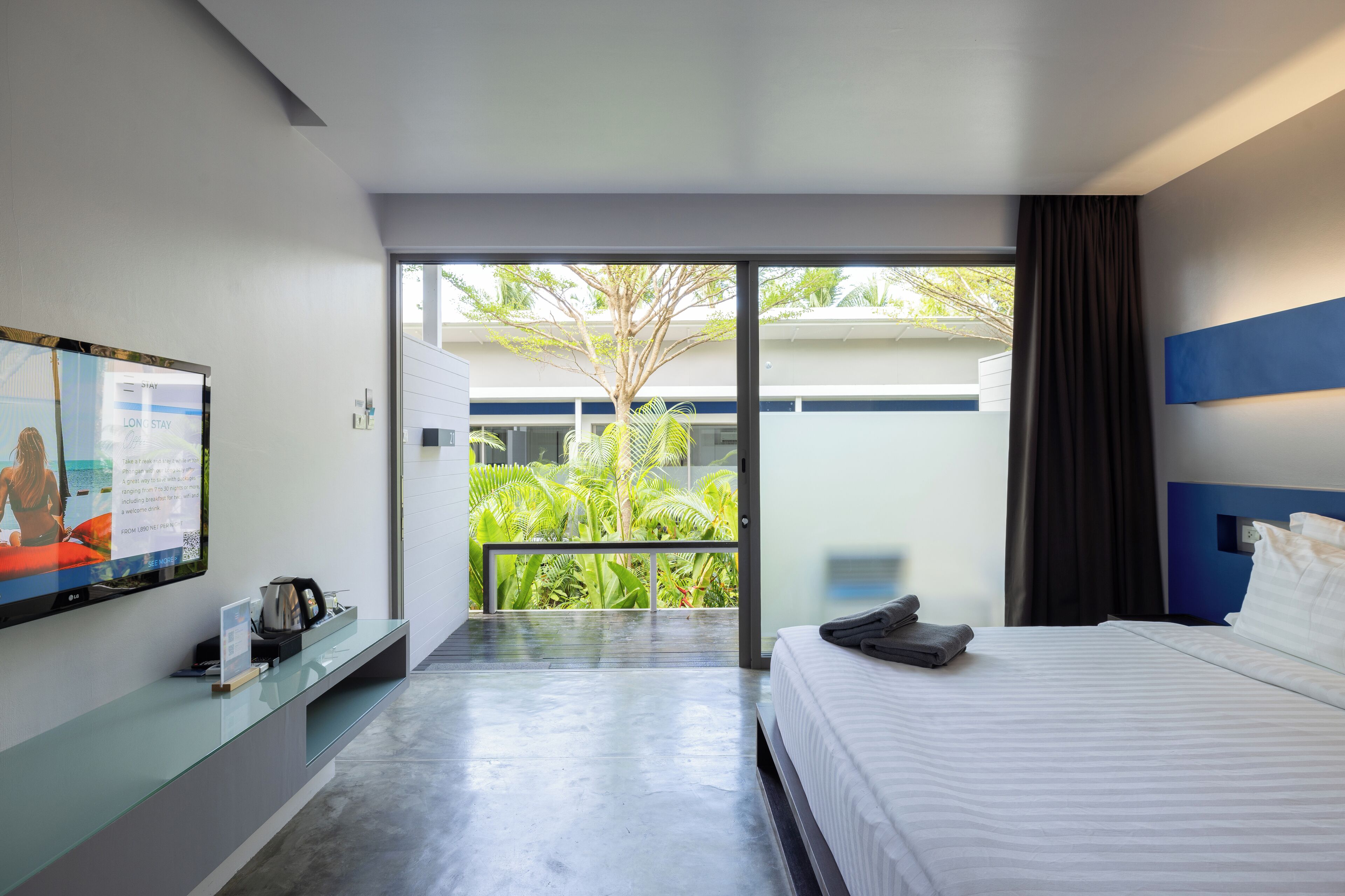 Une chambre d’hôtel moderne dotée d’un grand lit, d’une télévision à écran plat et d’un balcon offrant une vue sur la verdure.