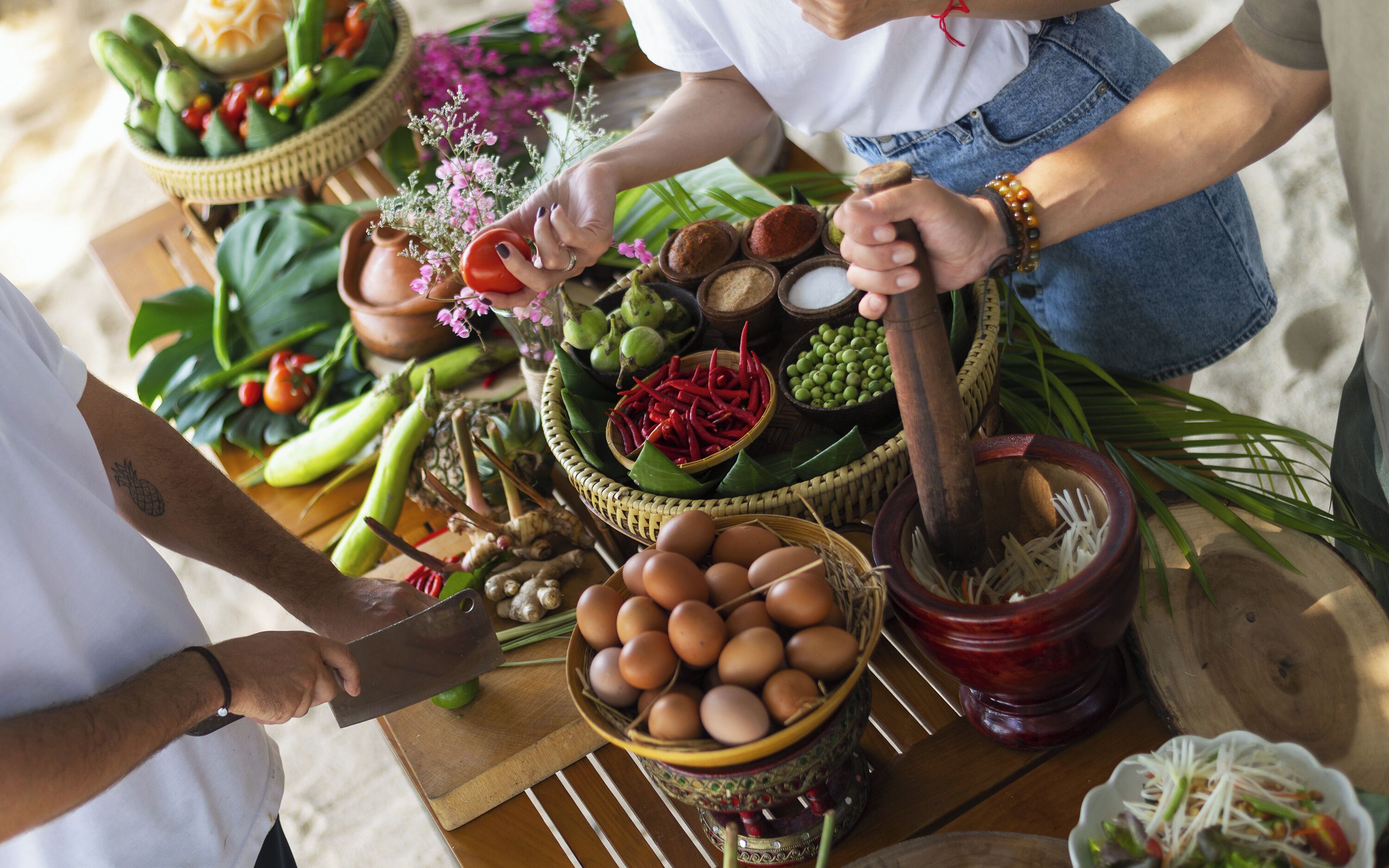 A person preparing food with various ingredients and tools on a wooden table.