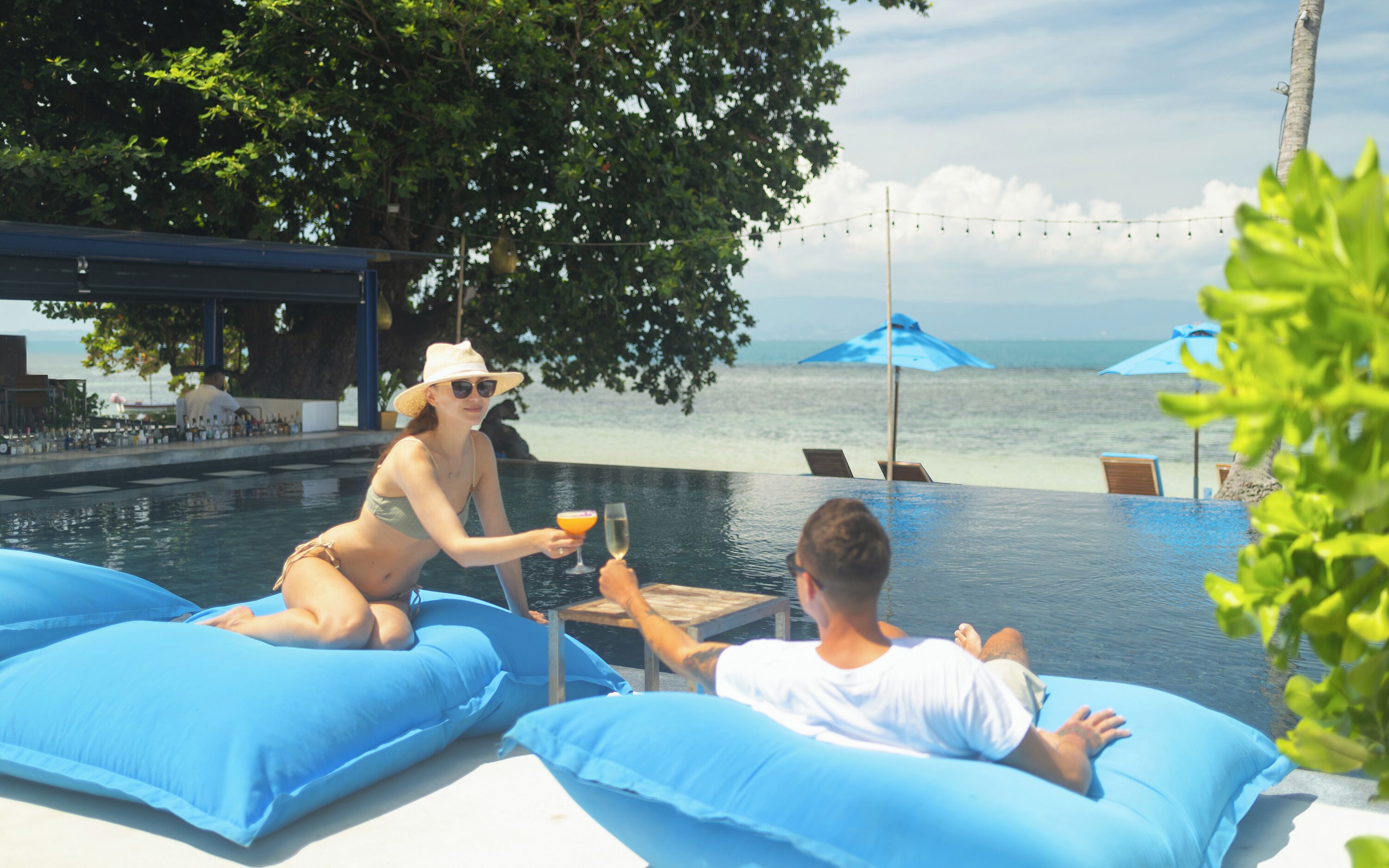 A poolside area with two blue lounge chairs, a person in a bikini, and another person in a white t-shirt.