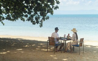 Una pareja cenando en una mesa en la playa, con vista al océano.