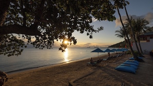 A beach with sunlit sand, lounge chairs, and umbrellas.