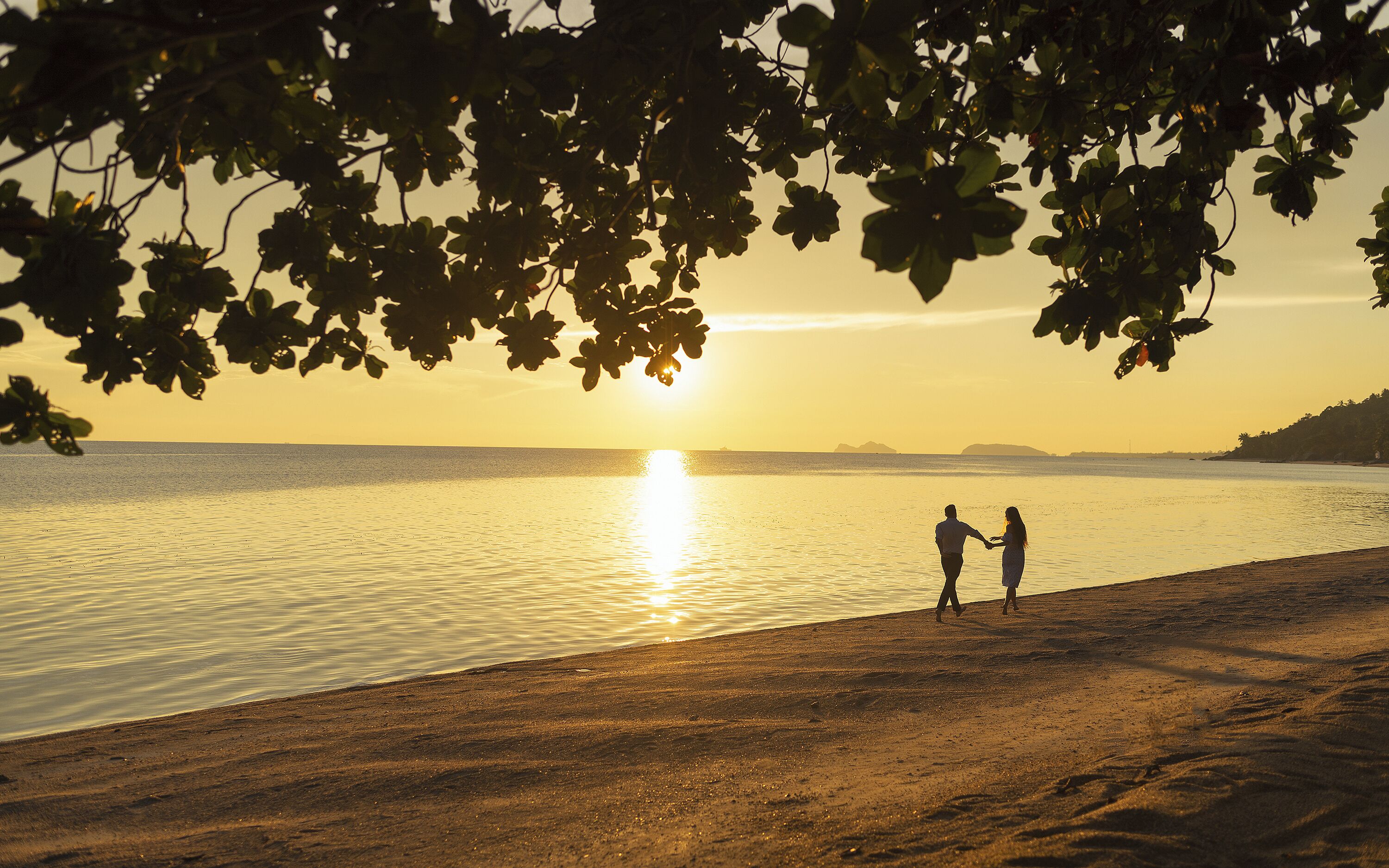 A beach scene with a sunset, two people holding hands, and a calm sea.