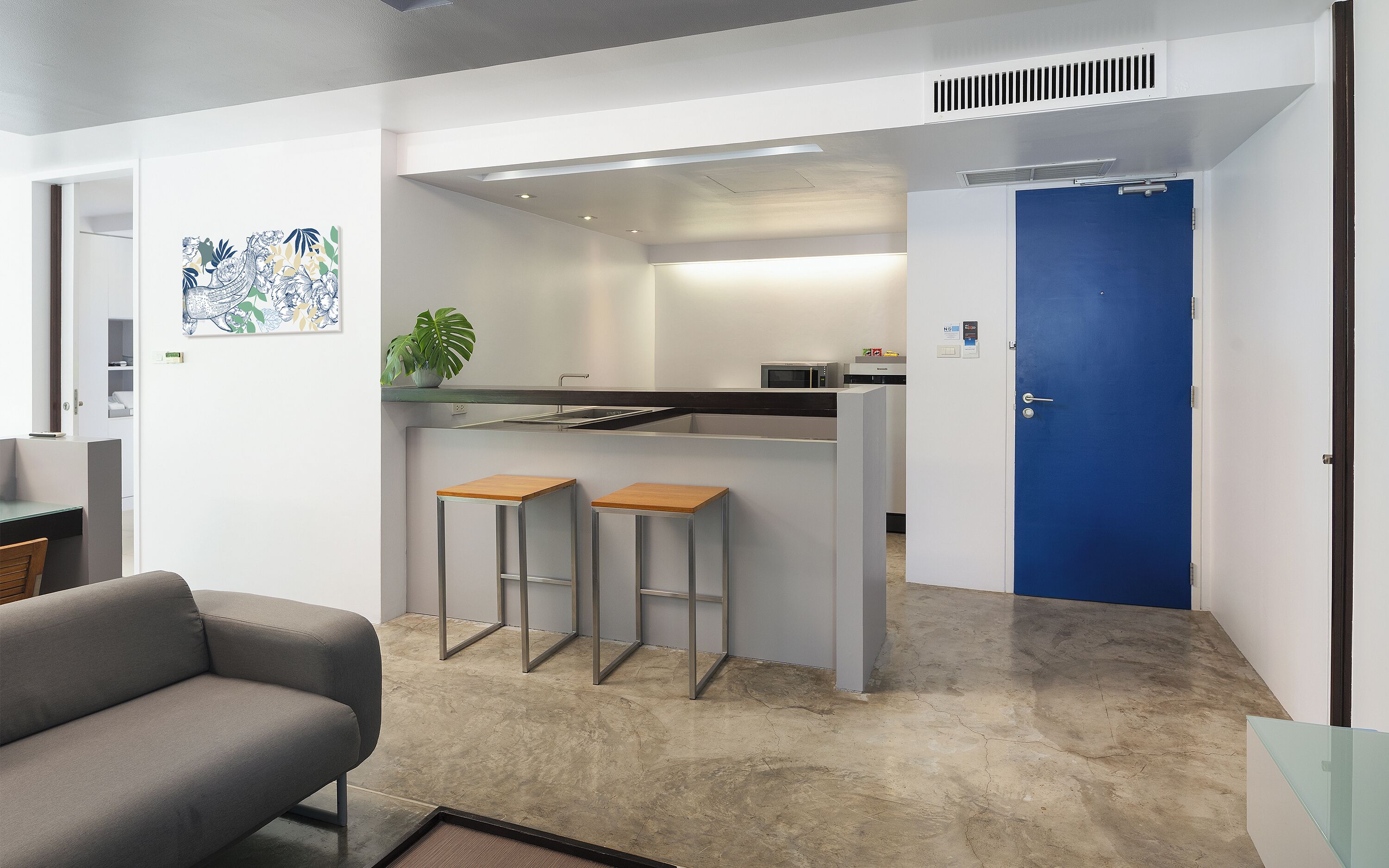 Une cuisine moderne avec une porte bleue, un coin bar avec des tabourets et un canapé gris.