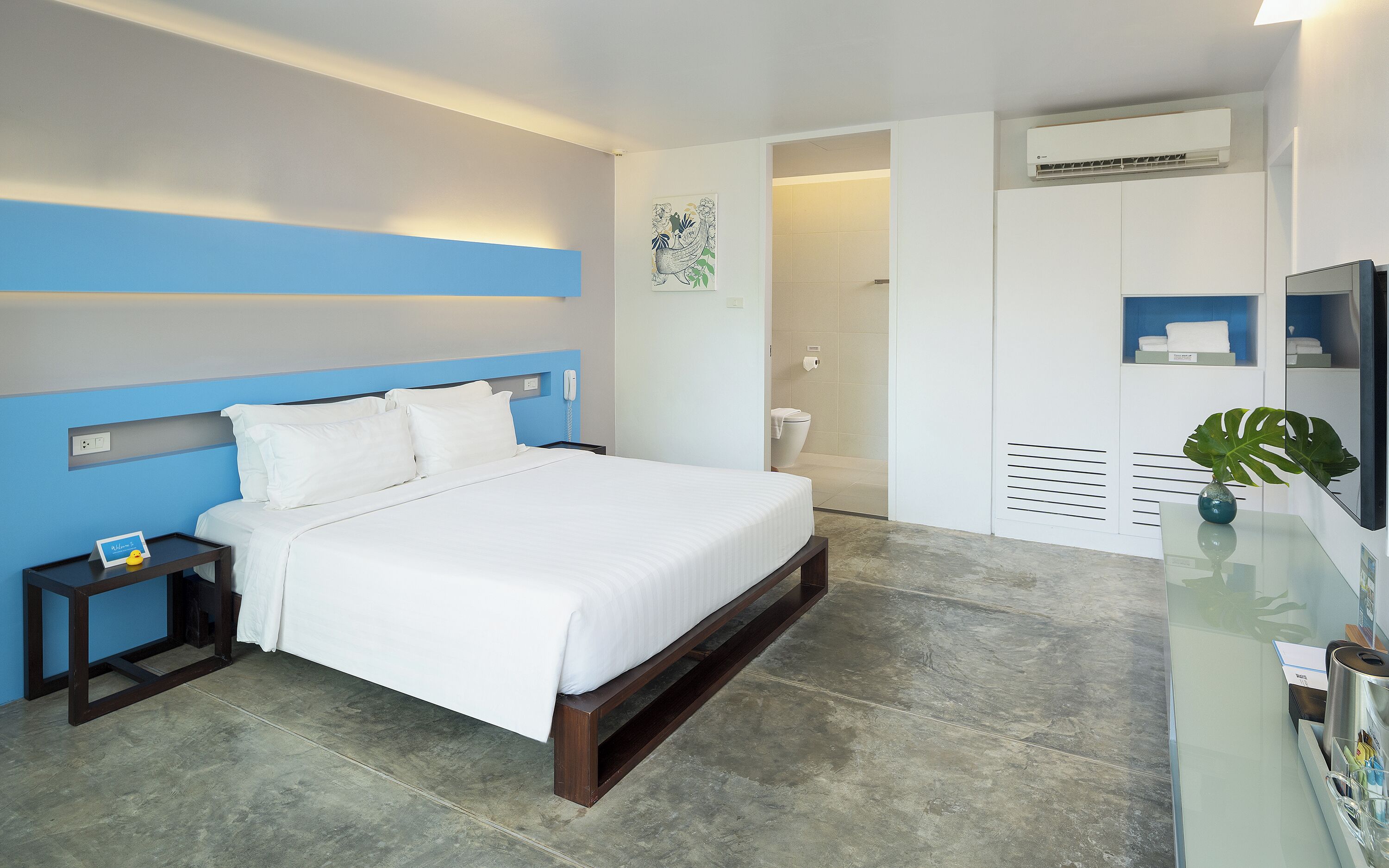 Une chambre d’hôtel moderne, équipée d’un lit, d’une table de chevet et d’une salle de bain visible à travers une porte ouverte.